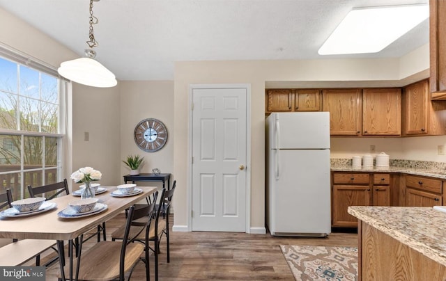 kitchen with light stone countertops, decorative light fixtures, freestanding refrigerator, light wood-style floors, and brown cabinetry