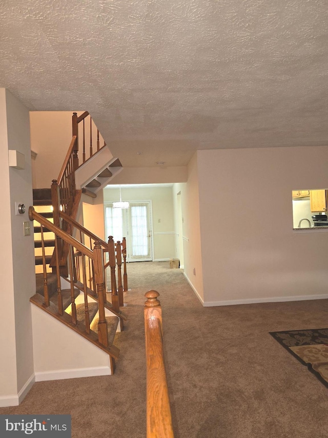 stairway featuring carpet flooring, a textured ceiling, and baseboards