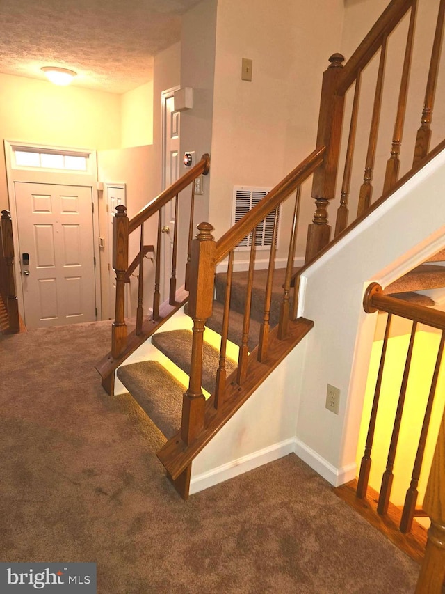 staircase featuring visible vents, baseboards, carpet, and a textured ceiling