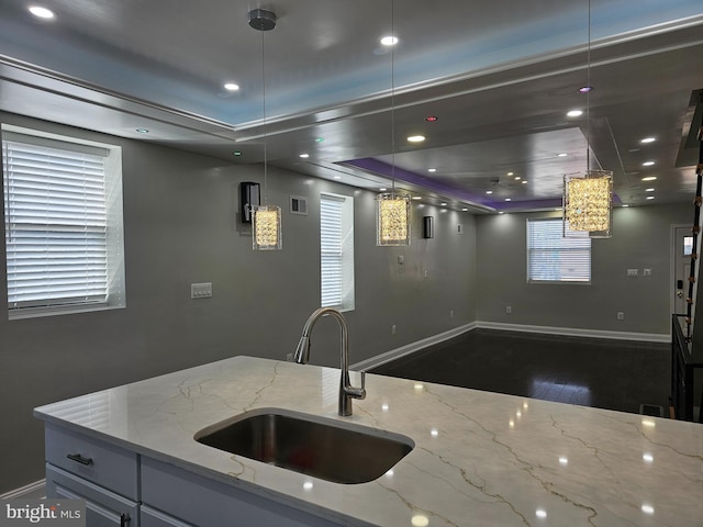 kitchen featuring light stone counters, wood finished floors, baseboards, visible vents, and a sink