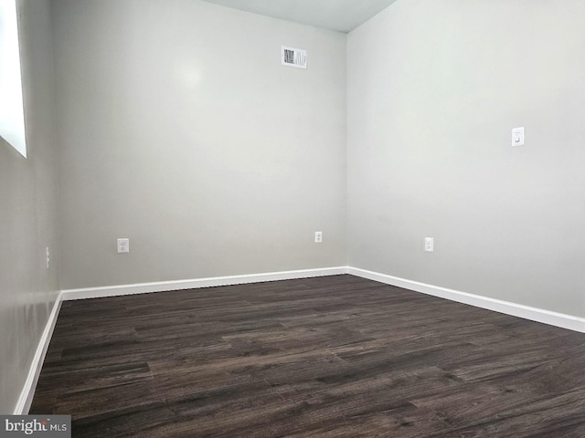 empty room featuring visible vents, baseboards, and dark wood-style flooring