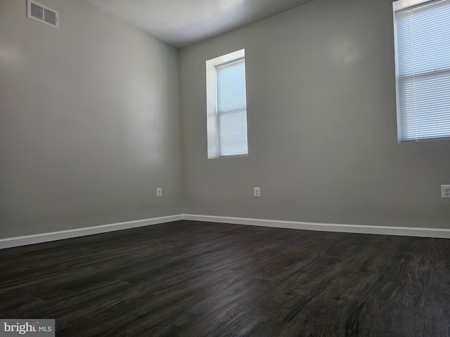 unfurnished room with dark wood-style floors, visible vents, and baseboards