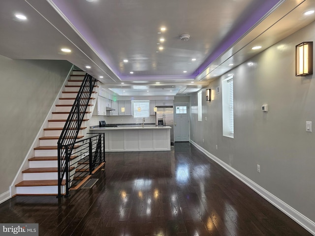 kitchen with baseboards, dark wood finished floors, a peninsula, white cabinetry, and a raised ceiling