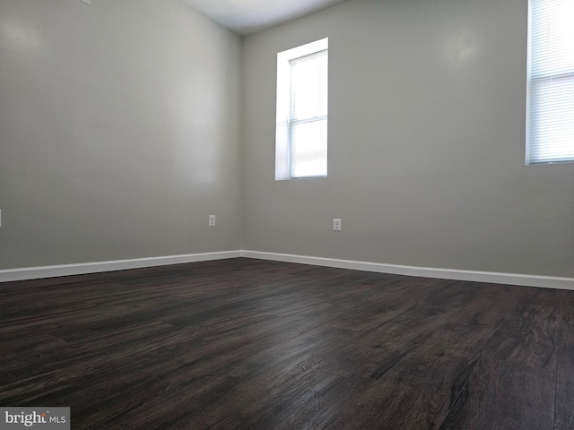 empty room with a wealth of natural light, baseboards, and dark wood-style flooring