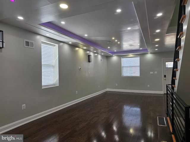 unfurnished living room featuring a tray ceiling, hardwood / wood-style flooring, baseboards, and visible vents