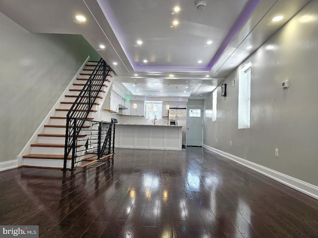 unfurnished living room featuring baseboards, stairway, a tray ceiling, recessed lighting, and dark wood-style flooring