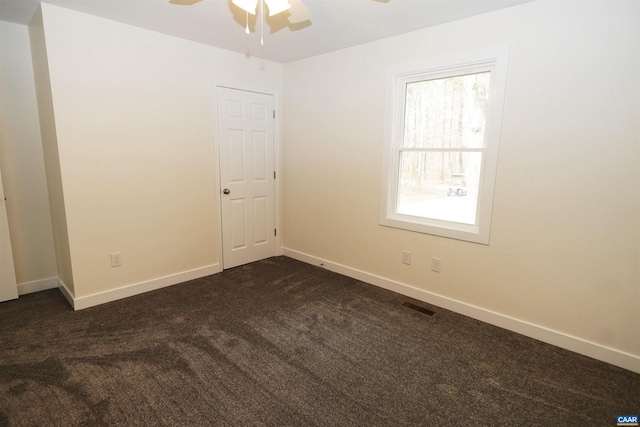 empty room featuring a ceiling fan, visible vents, dark carpet, and baseboards