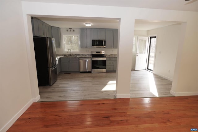 kitchen featuring baseboards, light wood finished floors, gray cabinets, a sink, and stainless steel appliances