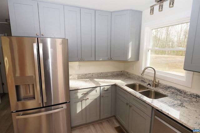 kitchen featuring gray cabinetry, light stone counters, light wood-style flooring, appliances with stainless steel finishes, and a sink