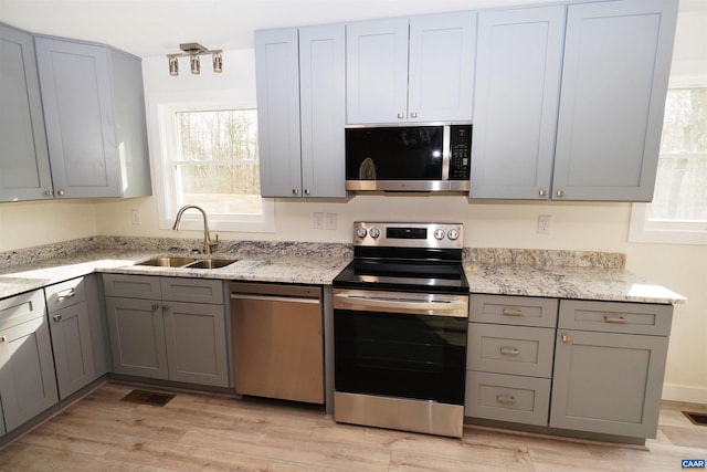 kitchen with light wood-type flooring, gray cabinets, a sink, appliances with stainless steel finishes, and light stone countertops