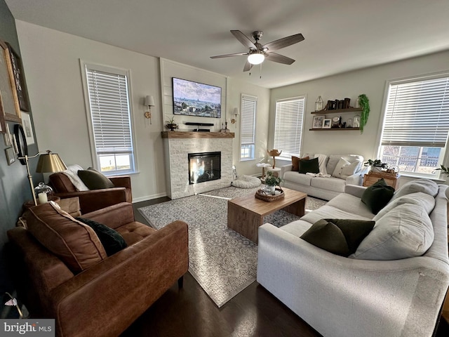 living area with a fireplace, baseboards, dark wood-type flooring, and ceiling fan