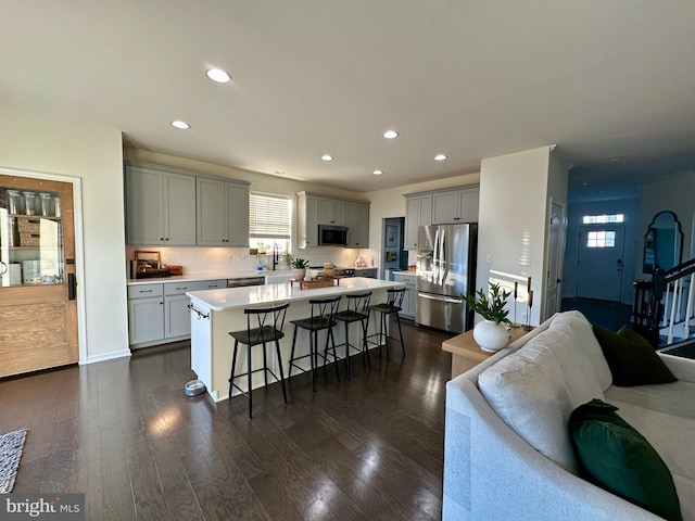 kitchen with gray cabinetry, open floor plan, a kitchen bar, light countertops, and stainless steel appliances