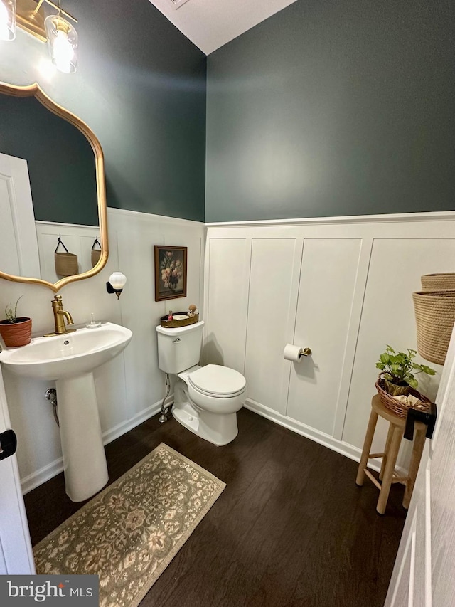 half bath with toilet, wood finished floors, a wainscoted wall, and a sink