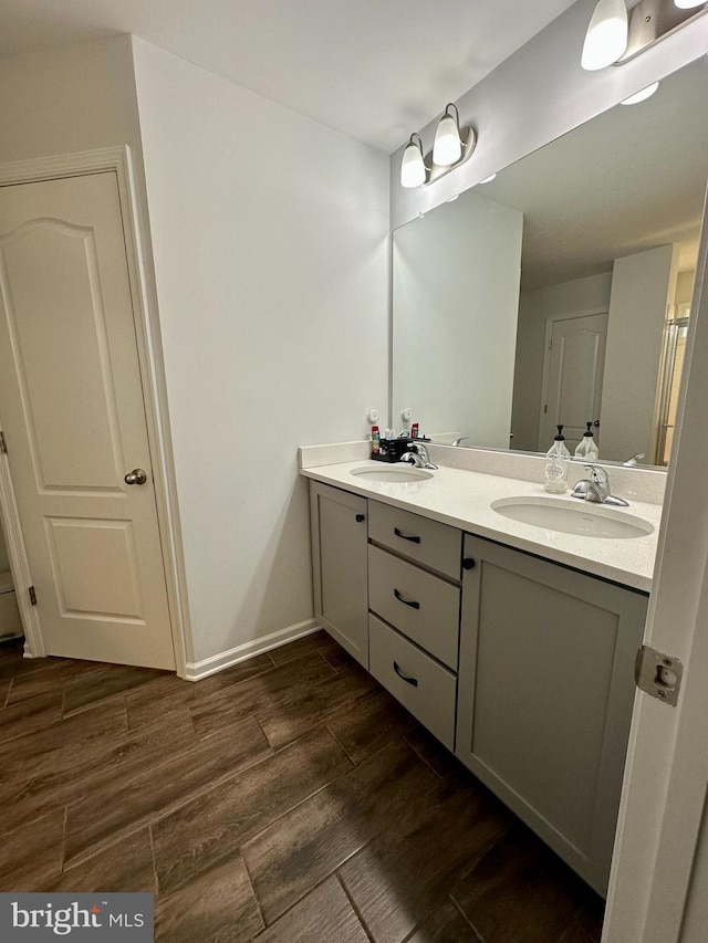 bathroom featuring double vanity, wood finished floors, baseboards, and a sink