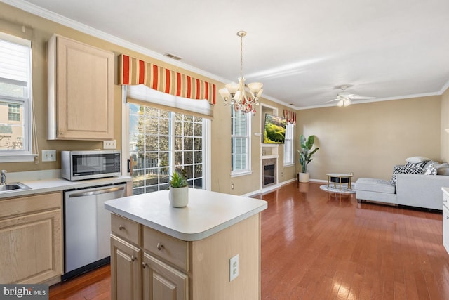 kitchen with light brown cabinetry, open floor plan, light countertops, ornamental molding, and stainless steel appliances