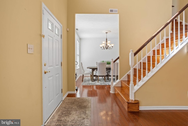 foyer entrance with hardwood / wood-style floors, baseboards, visible vents, stairs, and a chandelier