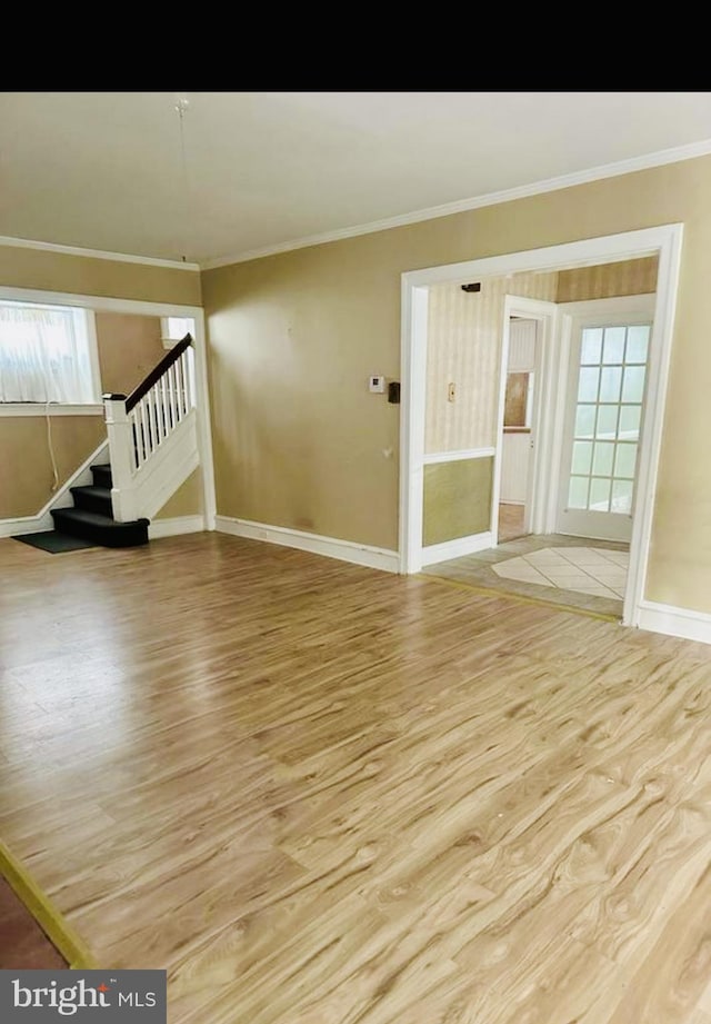 empty room featuring light wood-style flooring, baseboards, ornamental molding, and stairway