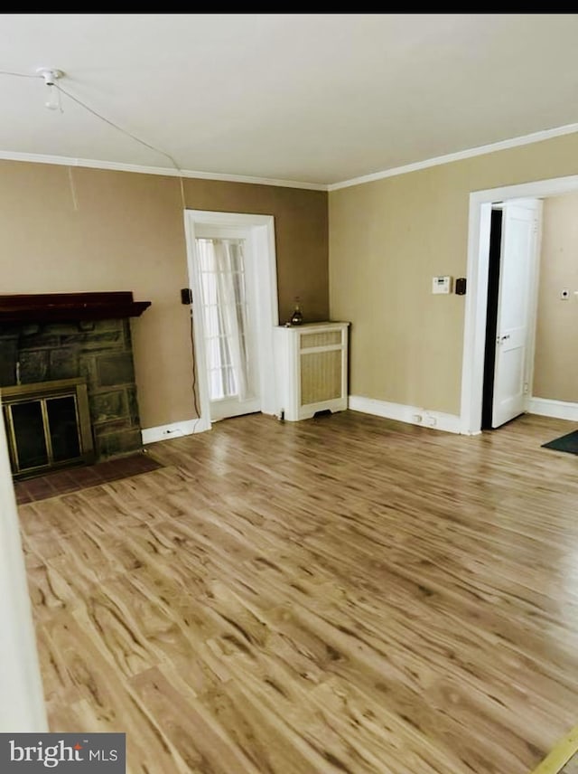 unfurnished living room with baseboards, a stone fireplace, wood finished floors, and ornamental molding