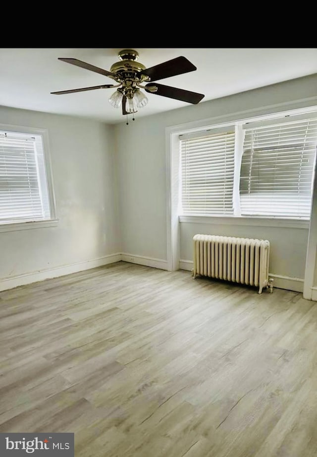 spare room featuring radiator heating unit, wood finished floors, baseboards, and a wealth of natural light