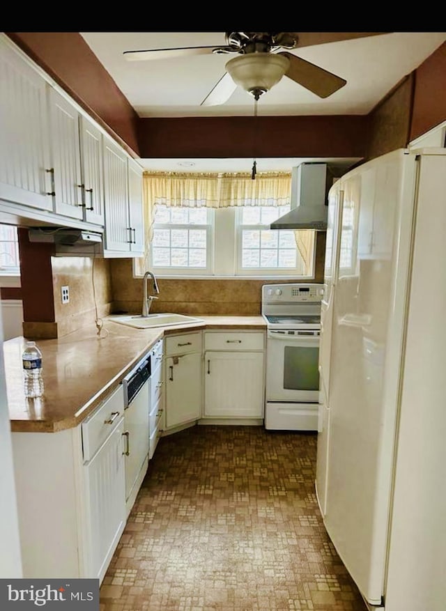 kitchen with white appliances, wall chimney range hood, white cabinets, and a sink