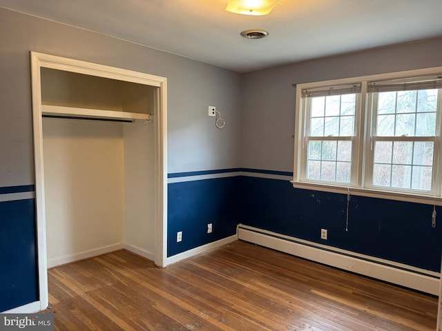 unfurnished bedroom featuring wood finished floors, visible vents, baseboards, a closet, and baseboard heating