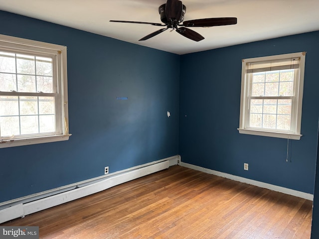 empty room featuring a wealth of natural light, a baseboard heating unit, baseboards, and hardwood / wood-style floors