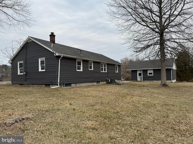 back of house with a yard, central air condition unit, a chimney, and a shingled roof