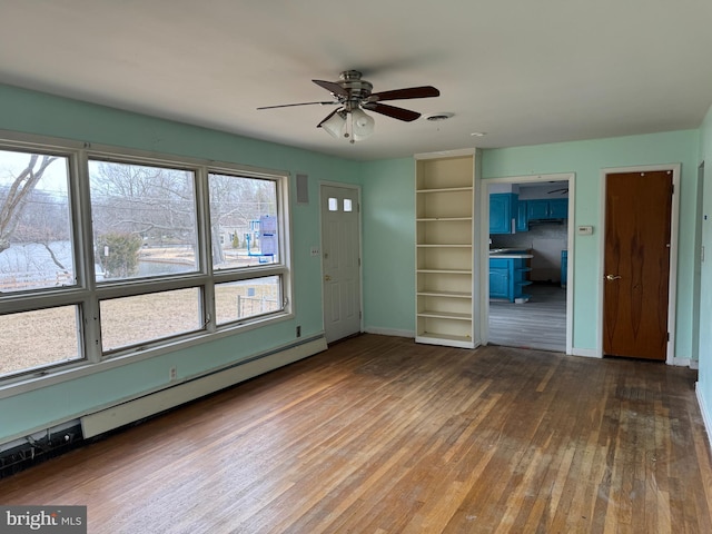 spare room featuring a baseboard heating unit, baseboards, wood-type flooring, and ceiling fan