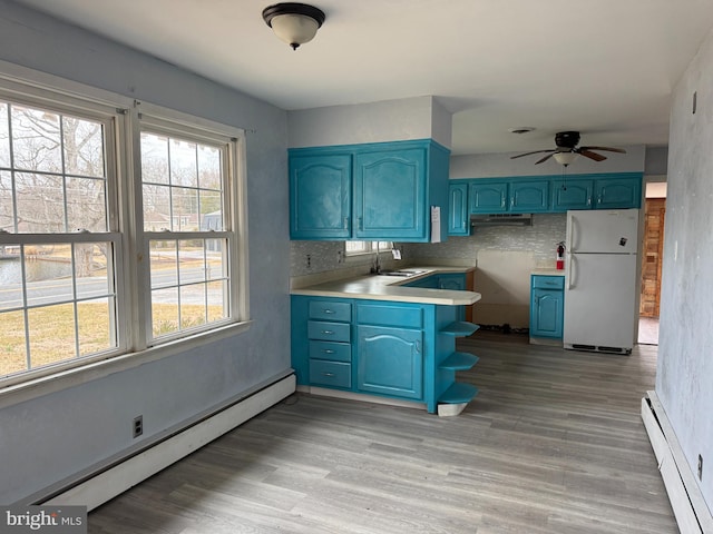 kitchen featuring freestanding refrigerator, a sink, a baseboard heating unit, blue cabinets, and baseboard heating