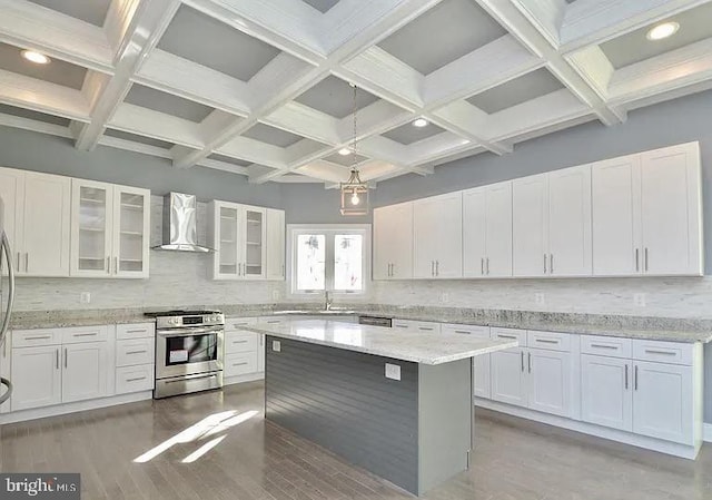 kitchen with stainless steel range with gas cooktop, wall chimney range hood, beamed ceiling, decorative backsplash, and white cabinetry