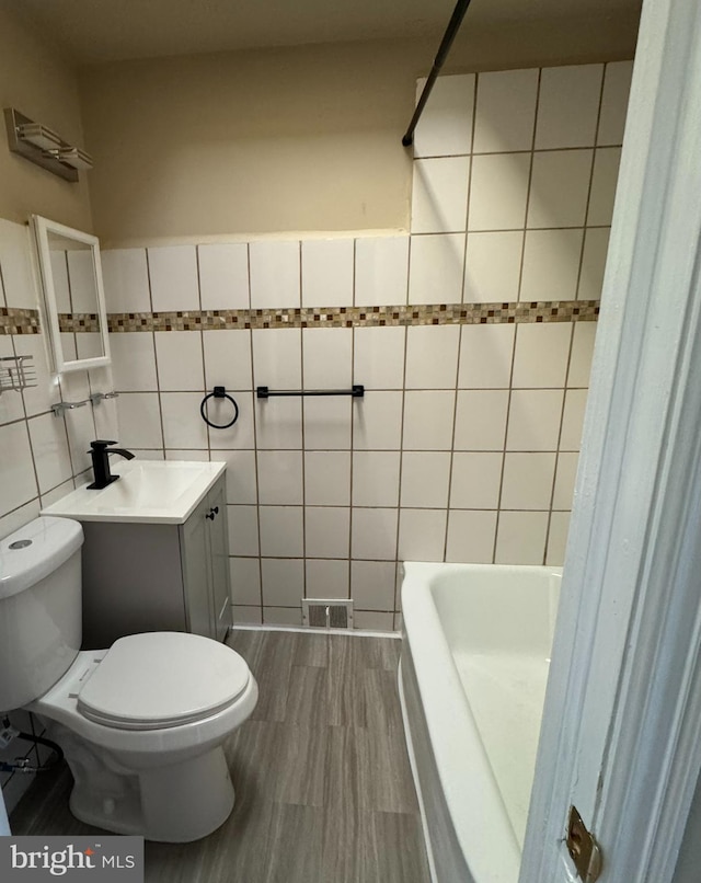 full bath featuring visible vents, toilet, a tub, and tile walls