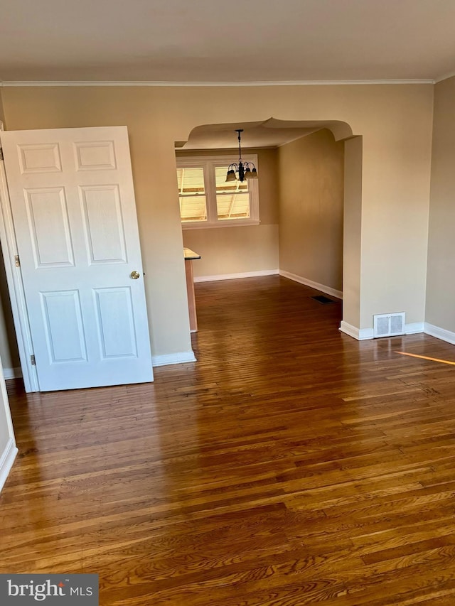 spare room with a notable chandelier, visible vents, ornamental molding, and dark wood-style flooring