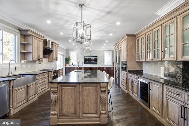 kitchen featuring beverage cooler, a center island with sink, a sink, crown molding, and wall chimney range hood