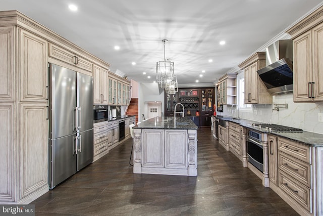 kitchen featuring cream cabinetry, an inviting chandelier, appliances with stainless steel finishes, wall chimney range hood, and decorative backsplash