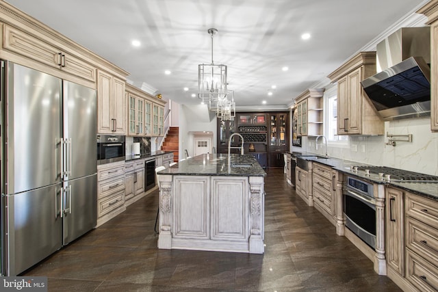 kitchen with recessed lighting, stainless steel appliances, cream cabinetry, crown molding, and wall chimney range hood