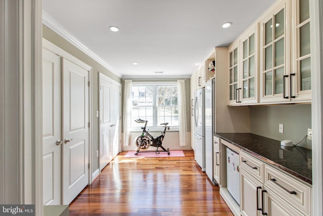 kitchen with dark stone countertops, freestanding refrigerator, light wood-style floors, crown molding, and glass insert cabinets