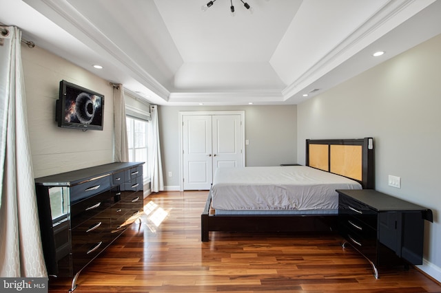 bedroom with a tray ceiling, wood finished floors, recessed lighting, a closet, and baseboards