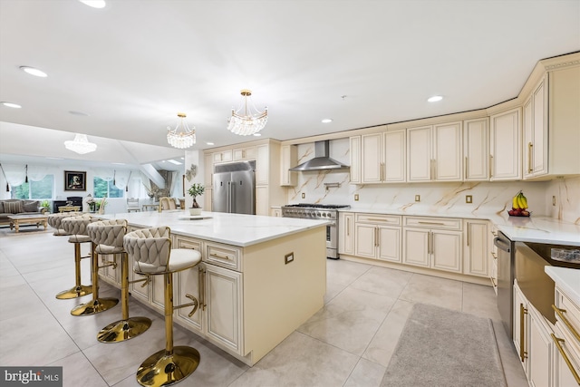 kitchen featuring premium appliances, cream cabinetry, wall chimney range hood, open floor plan, and a chandelier