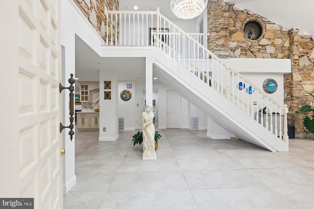 foyer entrance featuring visible vents, a towering ceiling, baseboards, a chandelier, and stairs