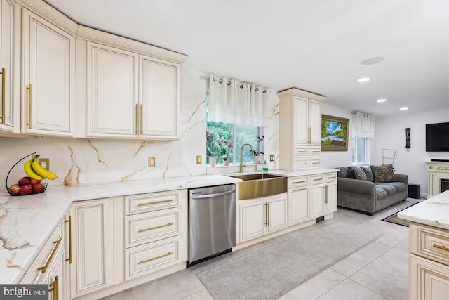 kitchen featuring light stone counters, a sink, cream cabinetry, dishwasher, and open floor plan