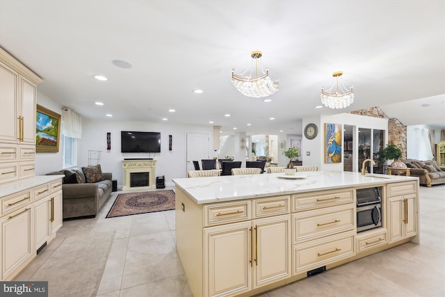 kitchen featuring stainless steel microwave, light stone countertops, a chandelier, open floor plan, and cream cabinetry