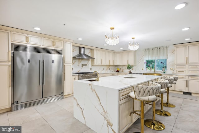 kitchen with light tile patterned floors, cream cabinetry, built in fridge, and wall chimney range hood