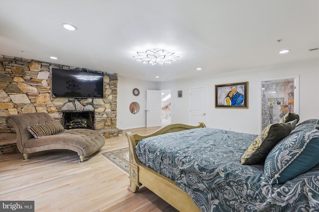 bedroom featuring recessed lighting, a stone fireplace, and wood finished floors