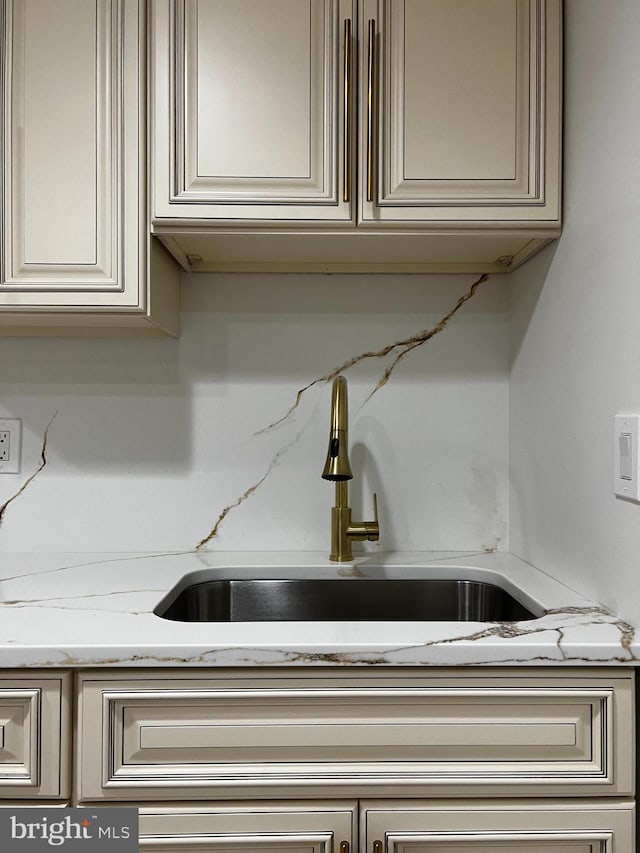 room details with a sink, light stone countertops, and cream cabinetry