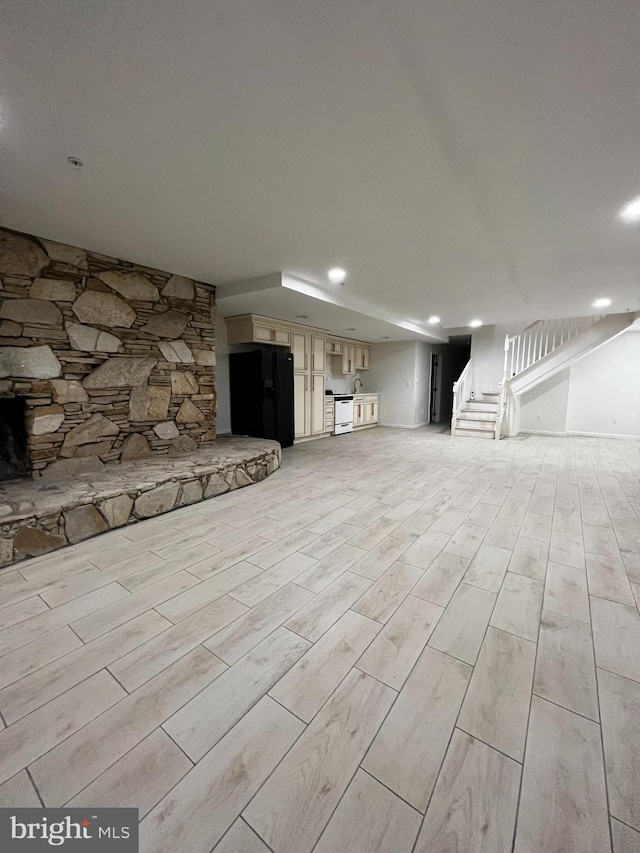 basement featuring black fridge with ice dispenser, stairway, and wood finish floors