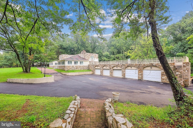 view of front of home with community garages, stairway, stone siding, and a front yard