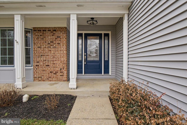 view of exterior entry with brick siding and covered porch