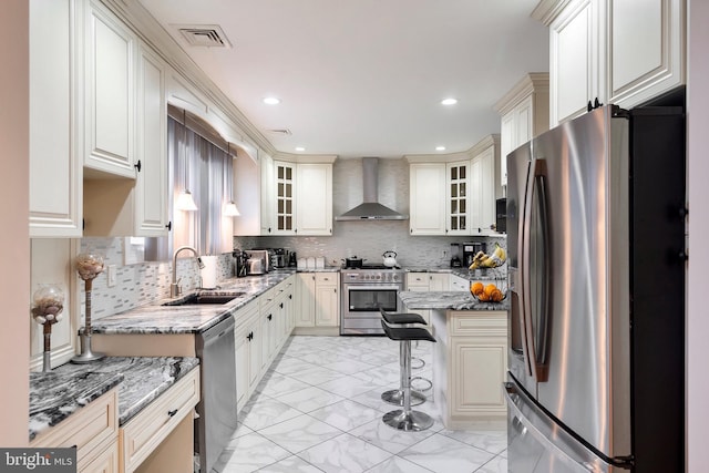 kitchen featuring a kitchen bar, marble finish floor, stainless steel appliances, wall chimney exhaust hood, and a sink