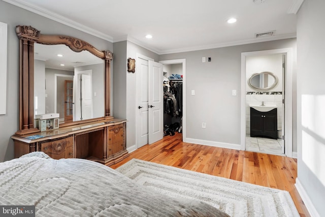 bedroom featuring baseboards, light wood finished floors, recessed lighting, a walk in closet, and crown molding