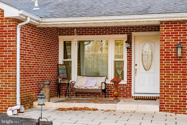 view of exterior entry with brick siding and roof with shingles